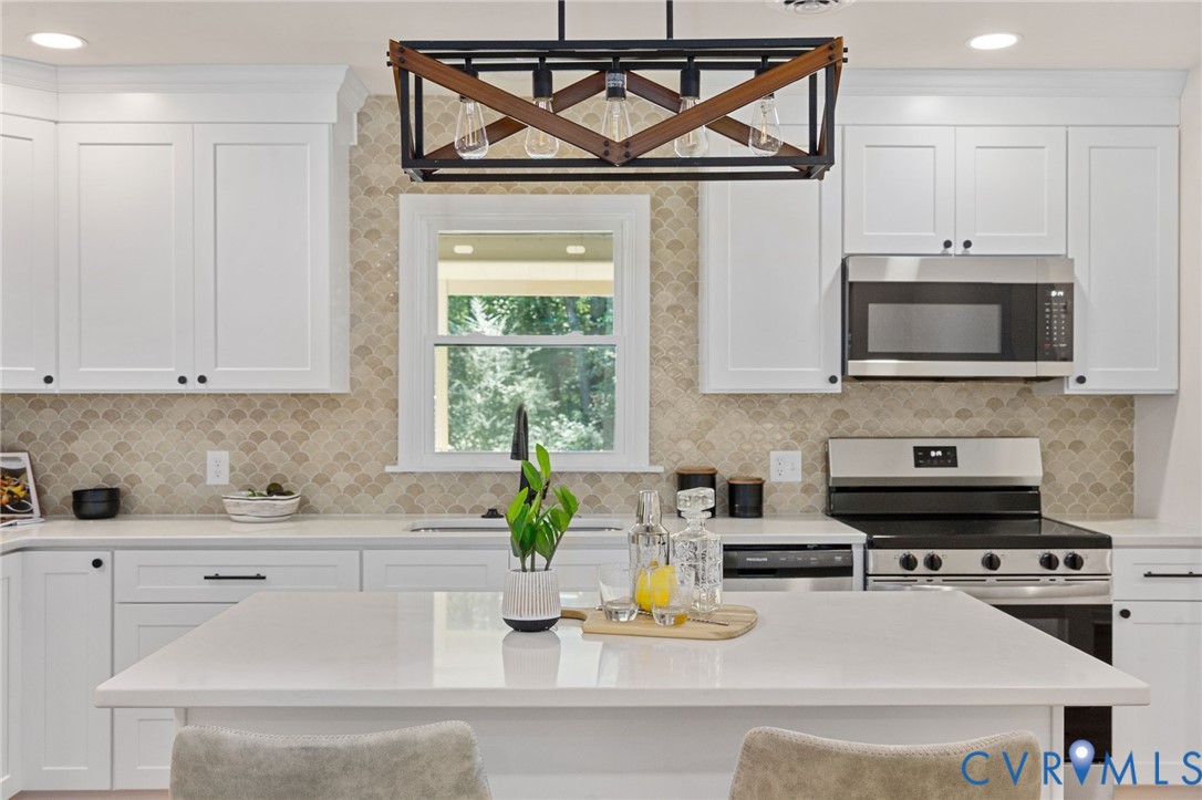 White shaker cabinetry, stainless steel appliances, neutral scallop tile backsplash, white countertop, and a contemporary chandelier