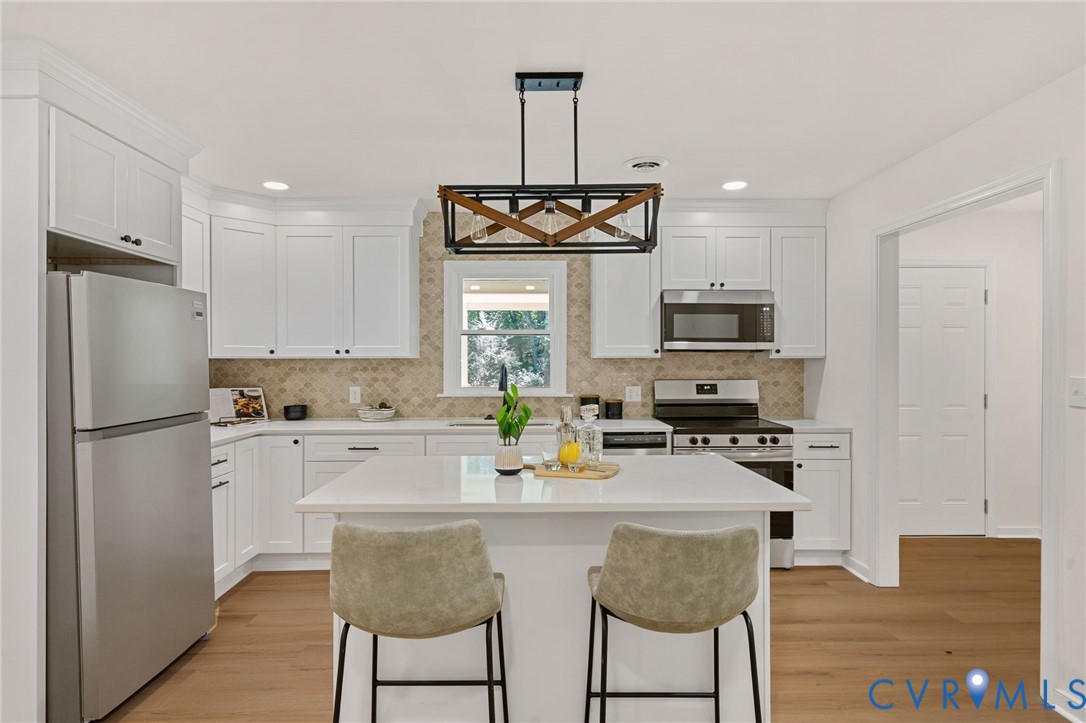 Kitchen featuring an island with countertop seating, stainless steel appliances, white cabinetry, a decorative tile backsplash, and wood-finish flooring