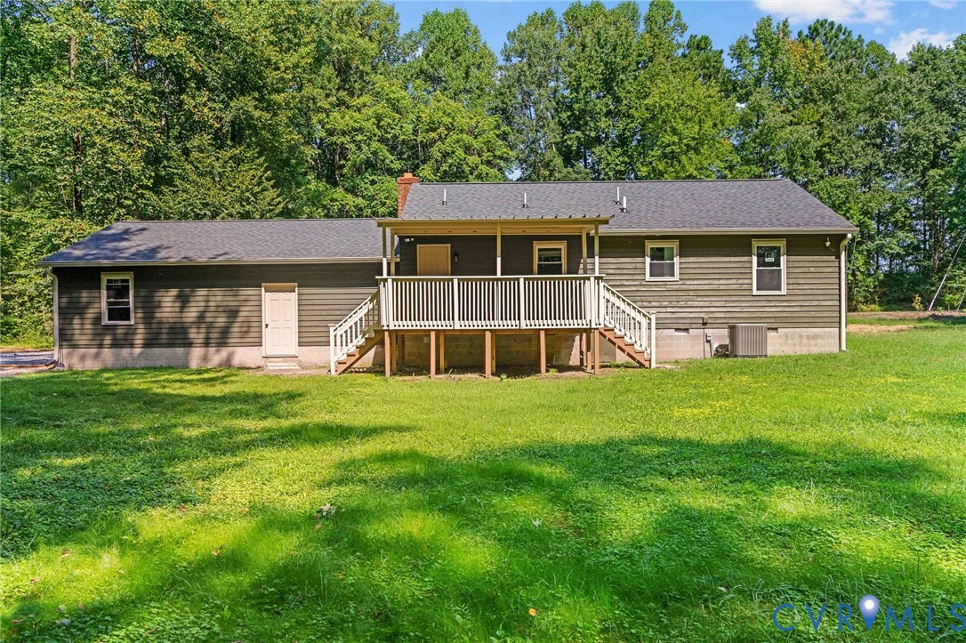 Rear exterior featuring a covered deck with white railings, a detached structure with siding and a white door, and a wooded backdrop