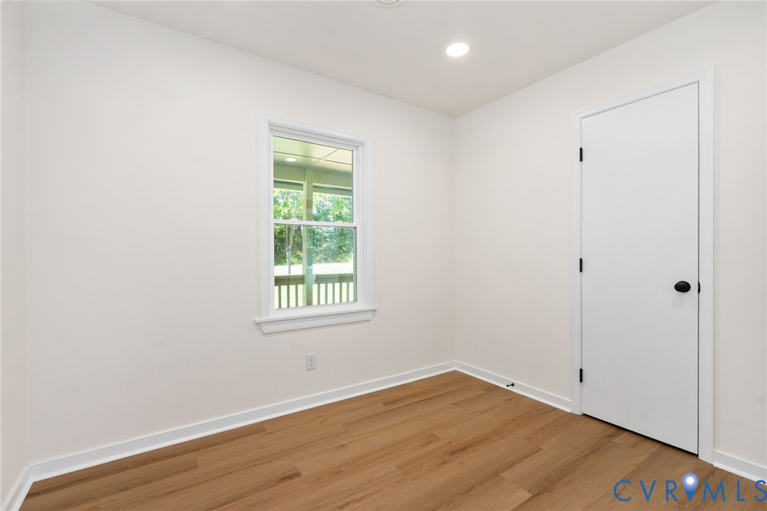 Recessed ceiling lighting, a single window, white trim, wood-finish flooring, and a white door with matte black hardware