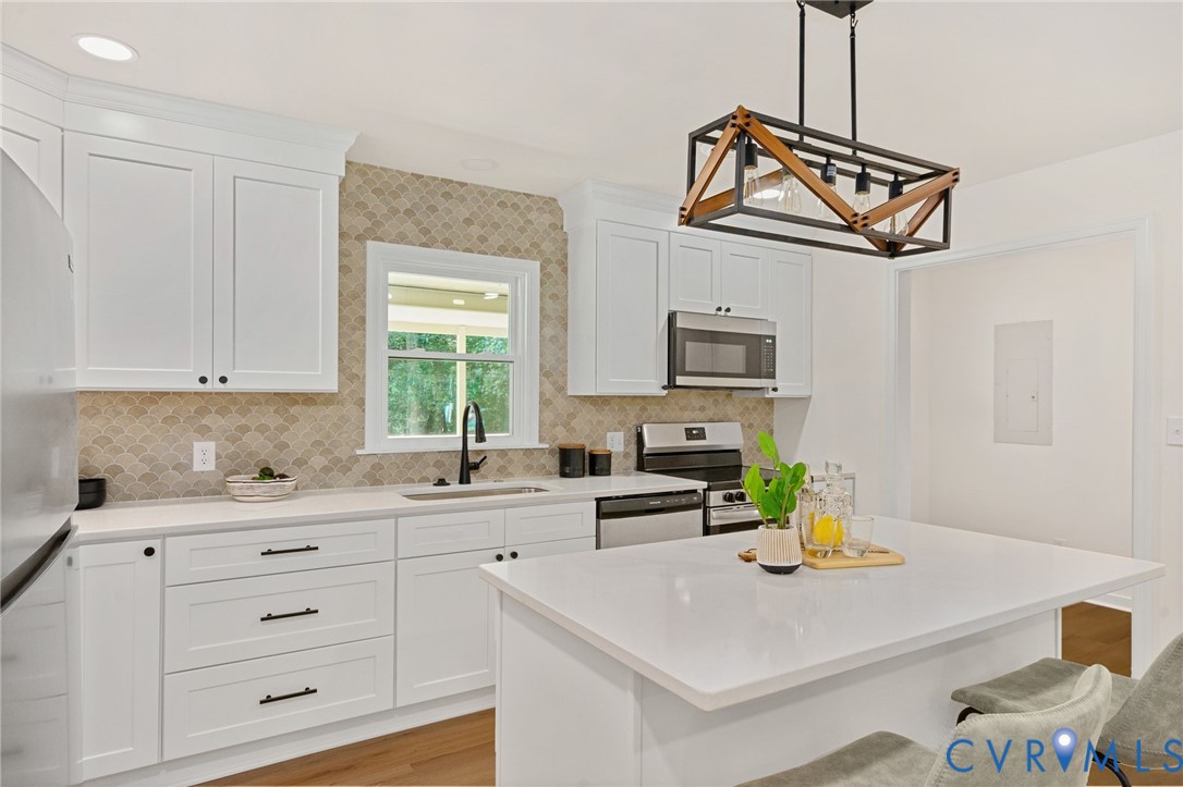 White shaker cabinetry, quartz countertops, stainless steel appliances, a decorative tiled backsplash, and wood-finish flooring