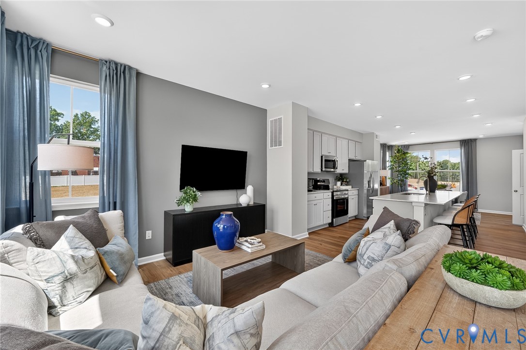 Open-concept living space featuring wood-finish flooring, recessed lighting, a modern kitchen with a large island, and stainless steel appliances
