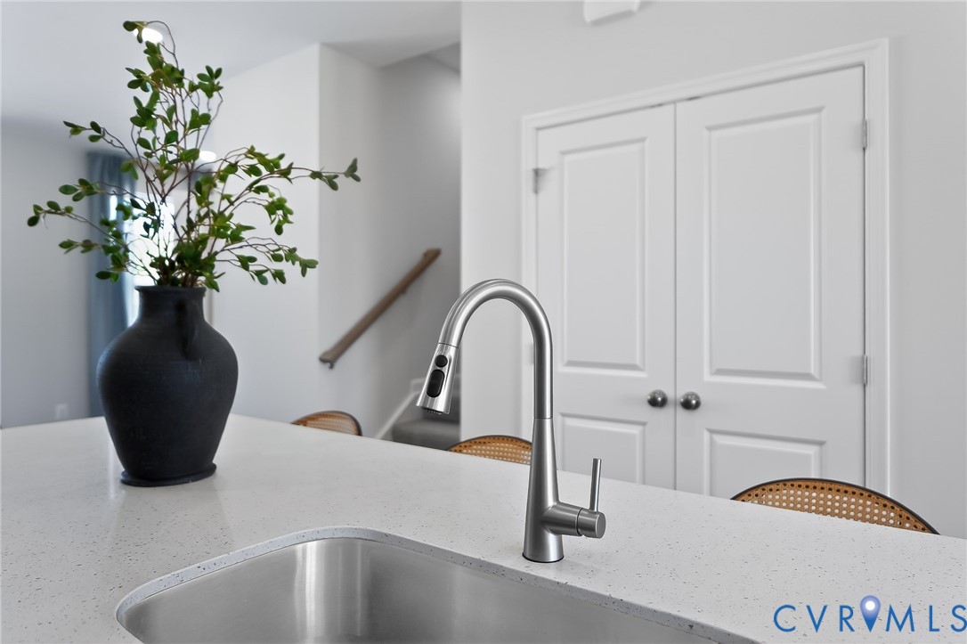 Stainless steel undermount sink with a gooseneck pull-down faucet, solid surface countertop, and white double panel doors