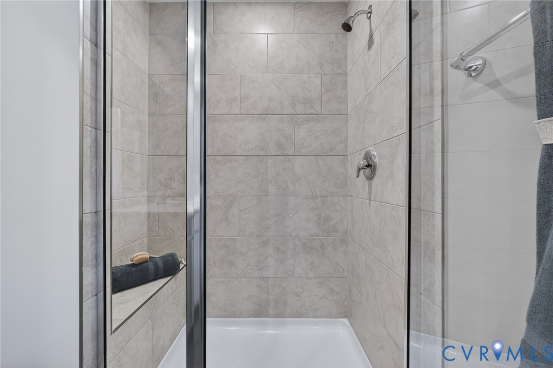 Glass-enclosed shower with a built-in bench, neutral tile surround, and chrome fixtures