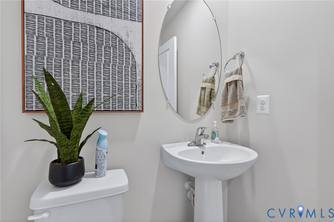 Pedestal sink with chrome faucet, oval wall-mounted mirror, and white toilet