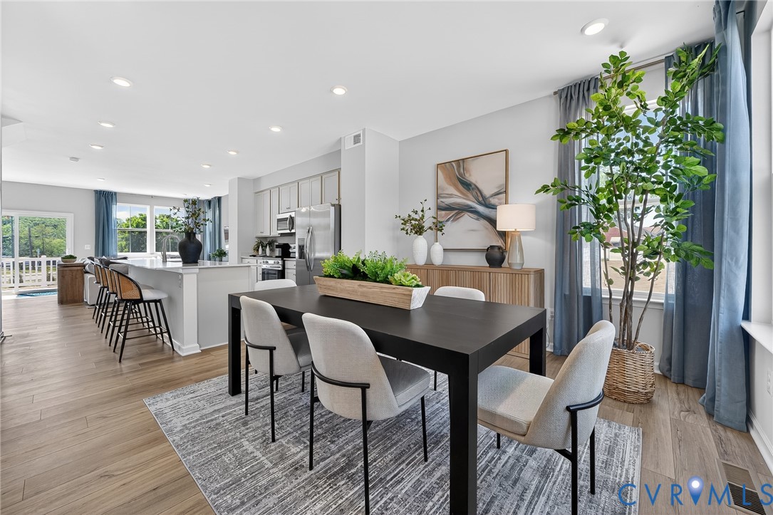 Wood-finish flooring throughout, recessed ceiling lighting, light gray kitchen cabinetry, stainless steel kitchen appliances, and a kitchen island with seating