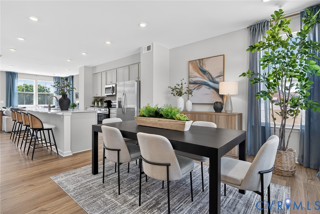 Spacious open-concept living area featuring wood-finish flooring, a kitchen island with seating, recessed lighting, and light gray cabinetry