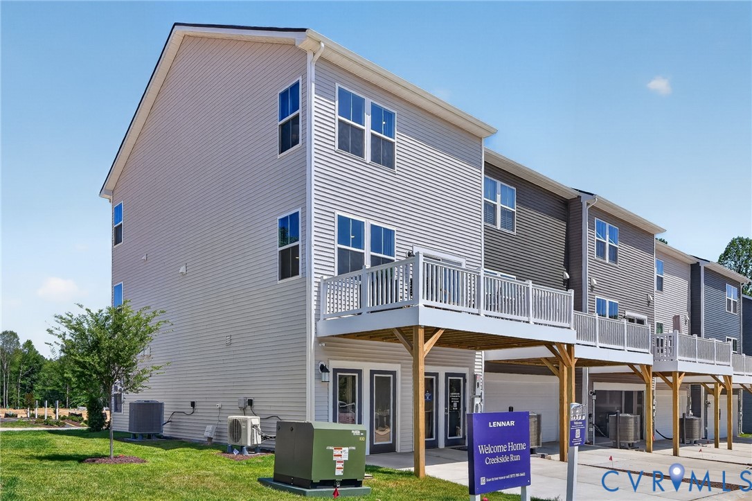 Multi-level townhome featuring light-colored siding, a white railing balcony, and a ground-level patio