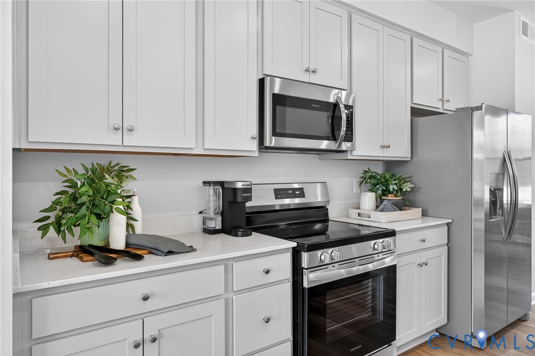 White shaker cabinetry, light-toned countertops, stainless steel appliances, and wood-finish flooring
