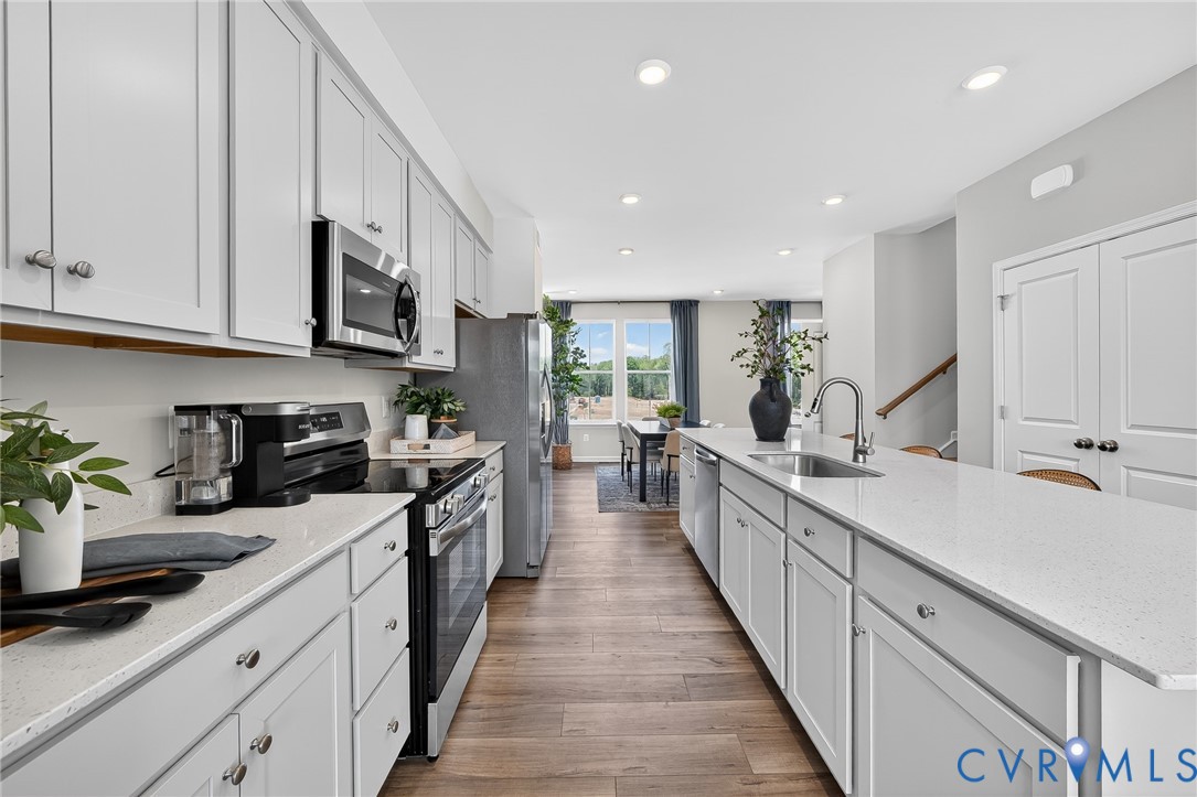 Galley kitchen featuring white cabinetry, light countertops, wood-finish flooring, stainless steel appliances, and recessed lighting