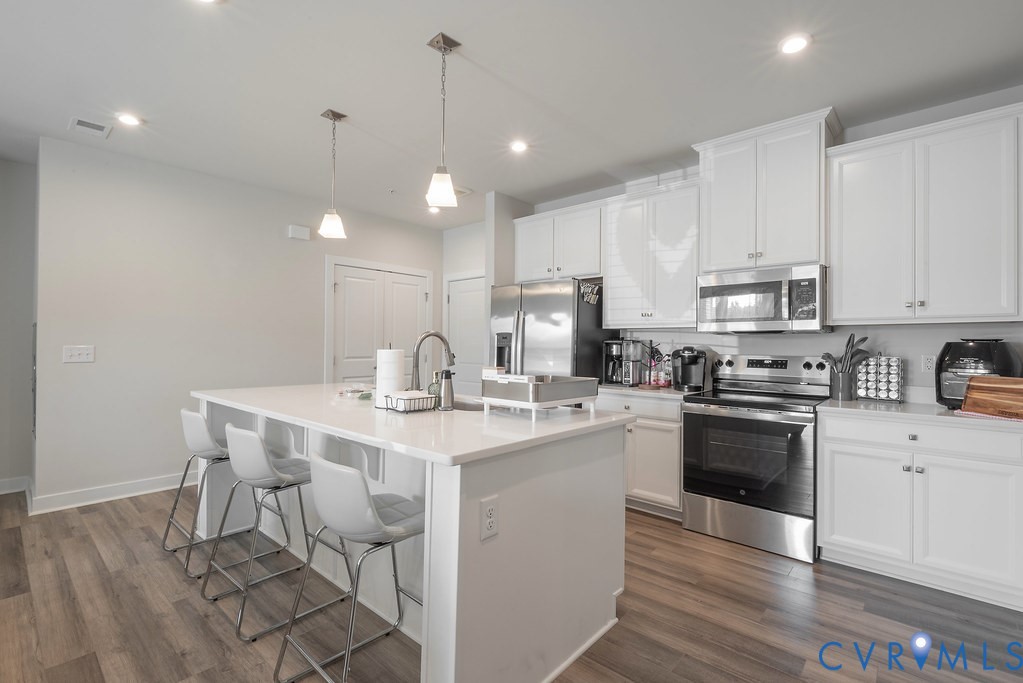 Kitchen featuring a large island with seating, white cabinetry, integrated stainless steel appliances, pendant lighting, and wood-finish flooring Kitchen featuring a large island with seating, white cabinetry, integrated stainless steel appliances, pendant lighting, and wood-finish flooring