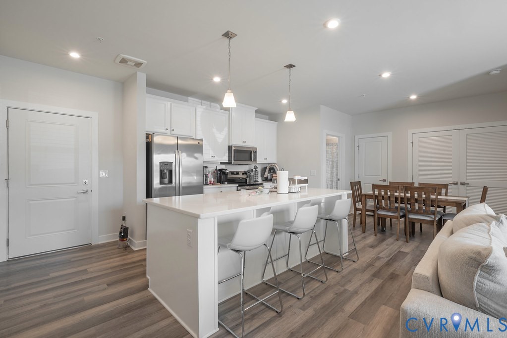 Open-concept living space featuring wood-finish flooring, recessed lighting, and a kitchen island with pendant lighting Open-concept living space featuring wood-finish flooring, recessed lighting, and a kitchen island with pendant lighting