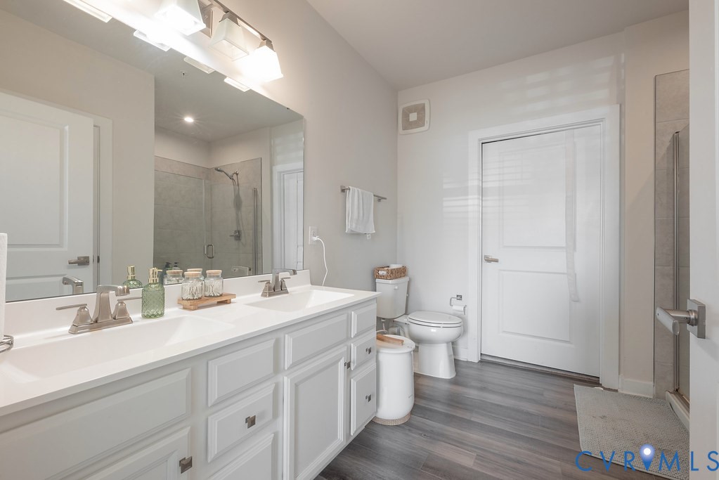 Double vanity with white cabinetry, wood-finish flooring, and a glass-enclosed shower