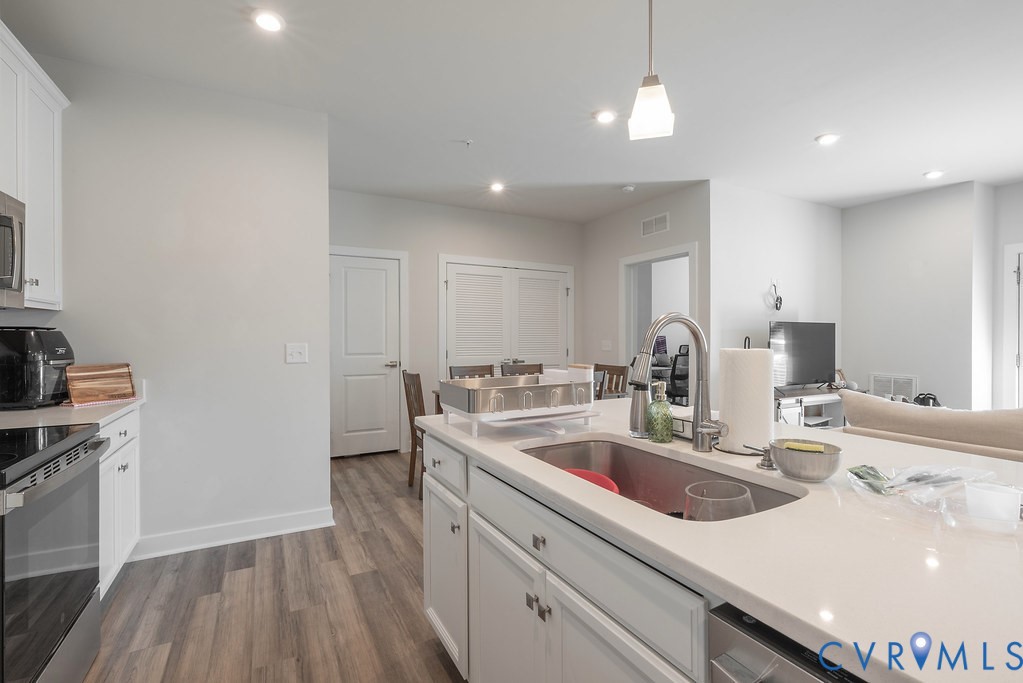 Kitchen featuring white cabinetry, stainless steel appliances, wood-finish flooring, recessed lighting, and an island with an integrated sink and gooseneck faucet