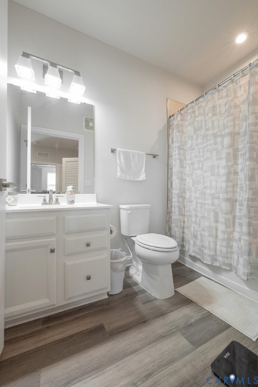 White vanity with integrated sink, wood-finish flooring, and a shower/tub combination with white tile surround