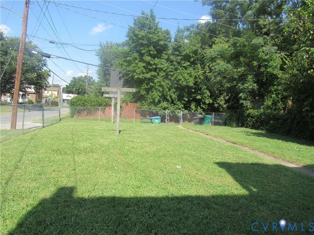 Expansive grassy yard with chain-link fencing, mature trees, and a privacy fence