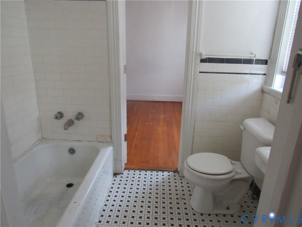 White subway tile wall surround, mosaic floor tile, white porcelain bathtub, and a white porcelain toilet