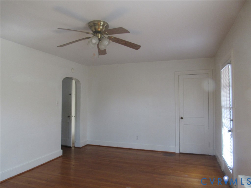 Hardwood flooring, arched doorway, ceiling fan with light fixture, window with blinds, white trim