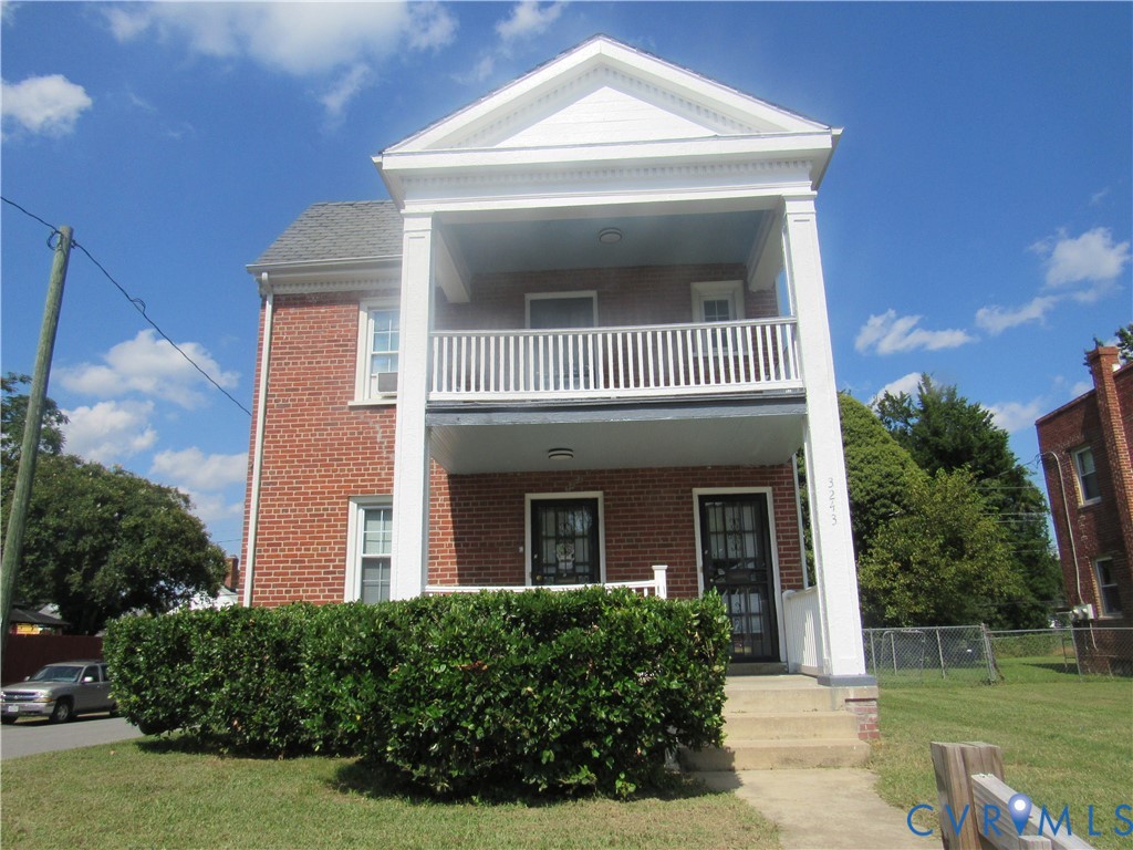 Brick exterior with a white two-story columned porch, upper-level balcony with white railing, and established front landscaping Brick exterior with a white two-story columned porch, upper-level balcony with white railing, and established front landscaping