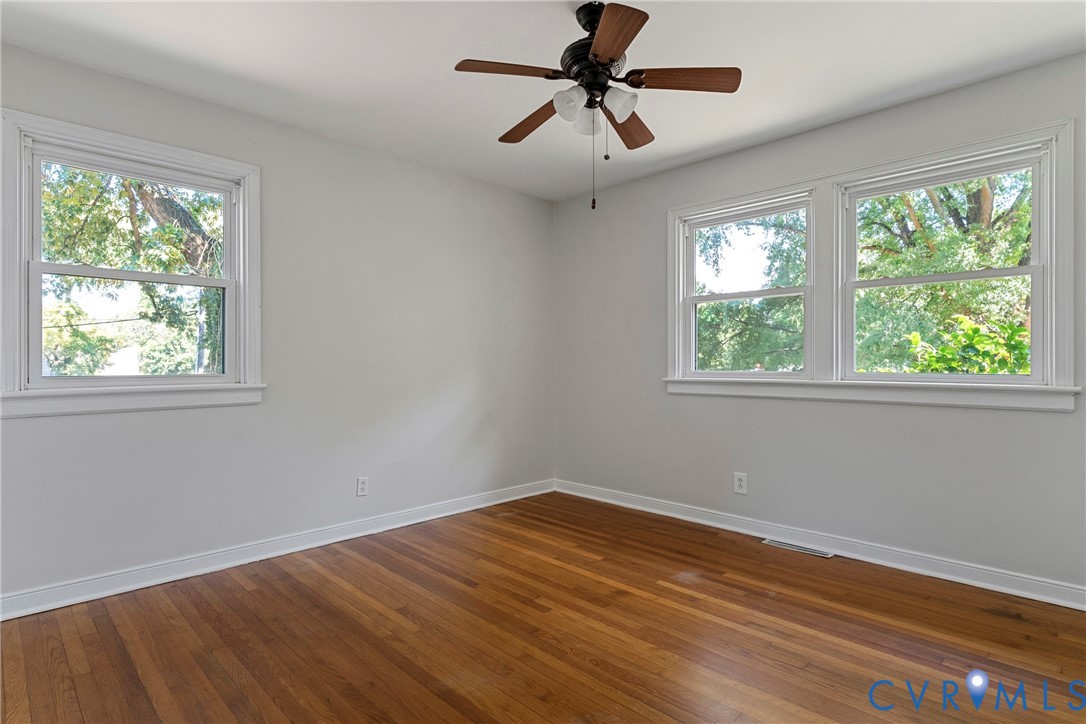 Hardwood flooring, painted walls, white trim, multiple windows, and a ceiling fan with integrated lighting