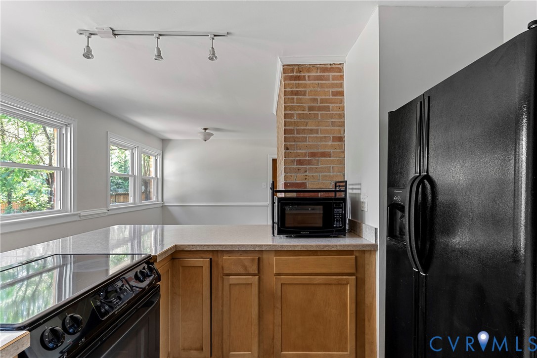 Kitchen featuring a black electric range, black refrigerator, wood cabinetry, and a light-toned countertop