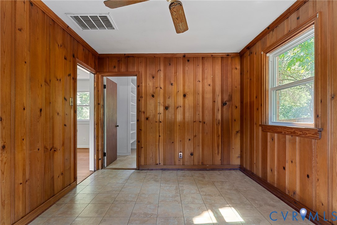 Wood panel walls, ceiling fan, ceramic tile flooring, and a window with natural light