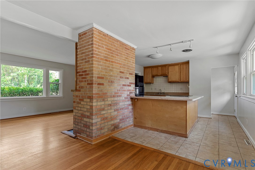 Brick accent wall, wood-finish flooring, kitchen with wood cabinetry, tile flooring, and multiple windows