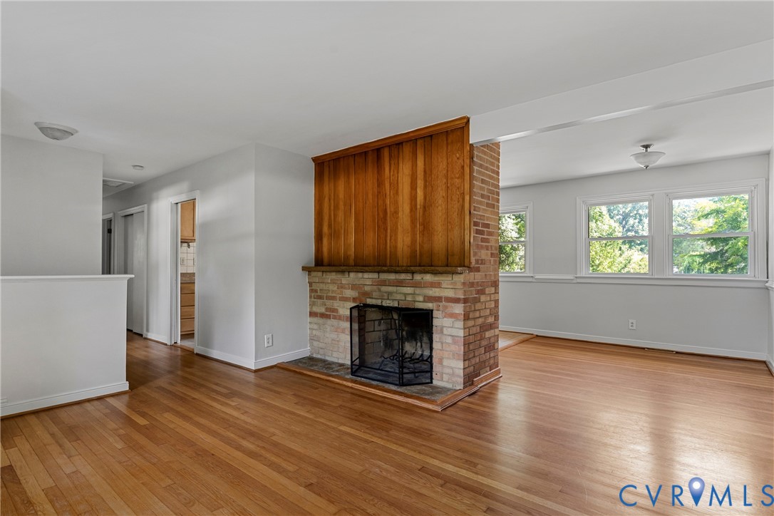 Wood-finish flooring throughout, brick fireplace with wood paneling, multiple windows, and a semi-flush ceiling light fixture