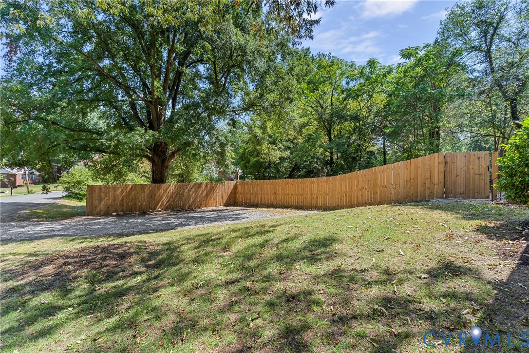 Expansive grassy area with a wood privacy fence and mature trees
