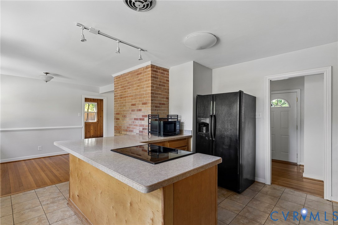 Kitchen island with a built-in cooktop, brick accent column, track lighting, and tile flooring