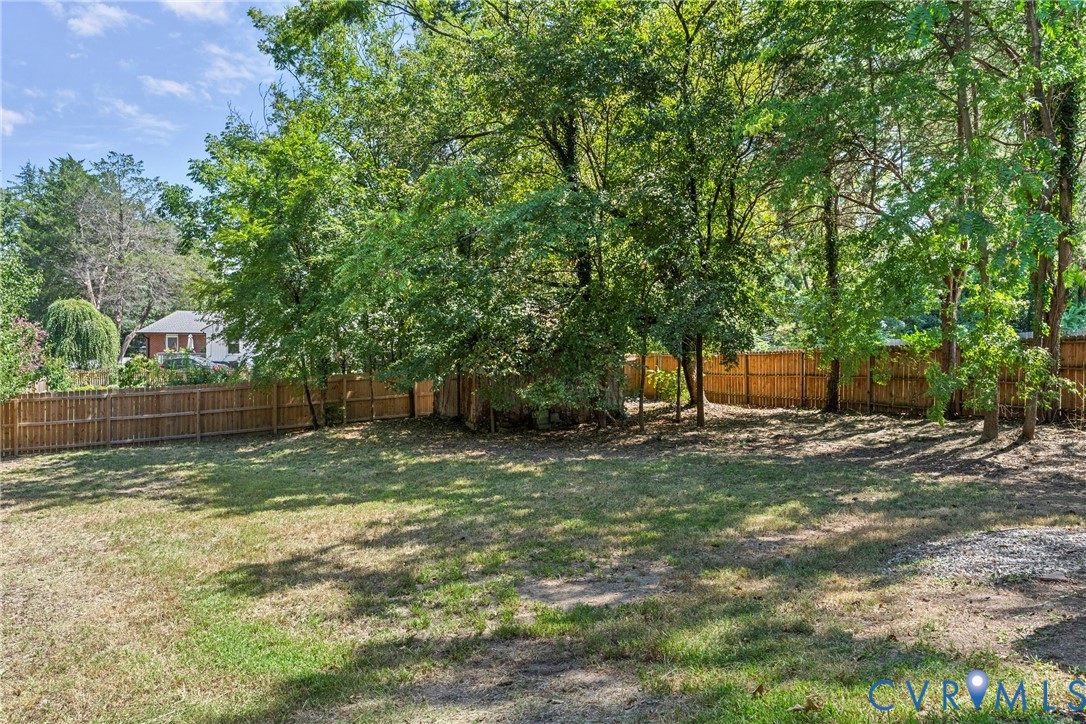 Expansive grassy area with a wood privacy fence and mature trees