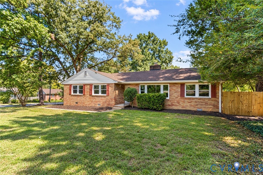 Brick exterior with white window frames and red shutters, featuring a brown shingle roof, mature landscaping, and a wooden privacy fence