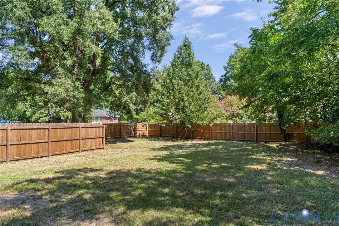 Expansive backyard space with a full privacy fence and mature trees