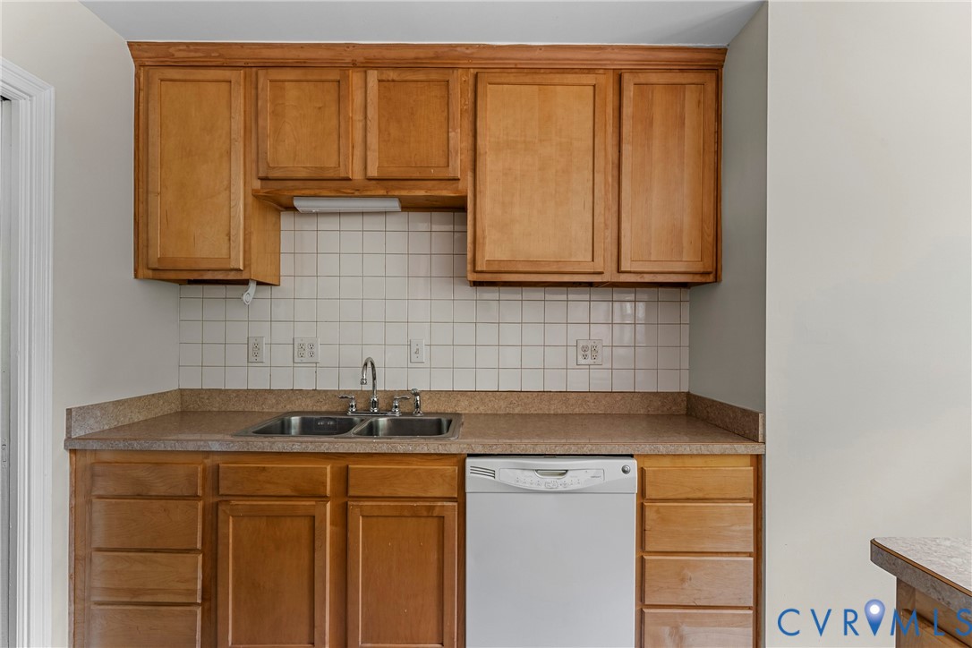 Kitchen featuring wood cabinetry, a double basin stainless steel sink, tile backsplash, and a built-in dishwasher