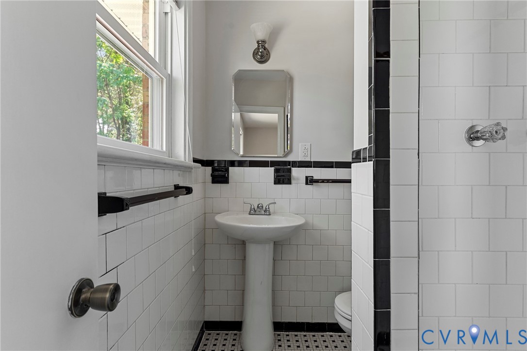 Pedestal sink with chrome faucet, white subway tile, black accent tile, and a wall-mounted mirror