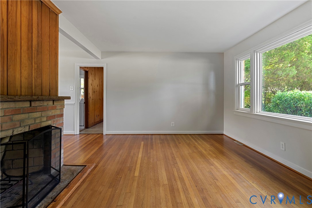 Brick fireplace with a wood panel surround, wood-finish flooring, and bright windows
