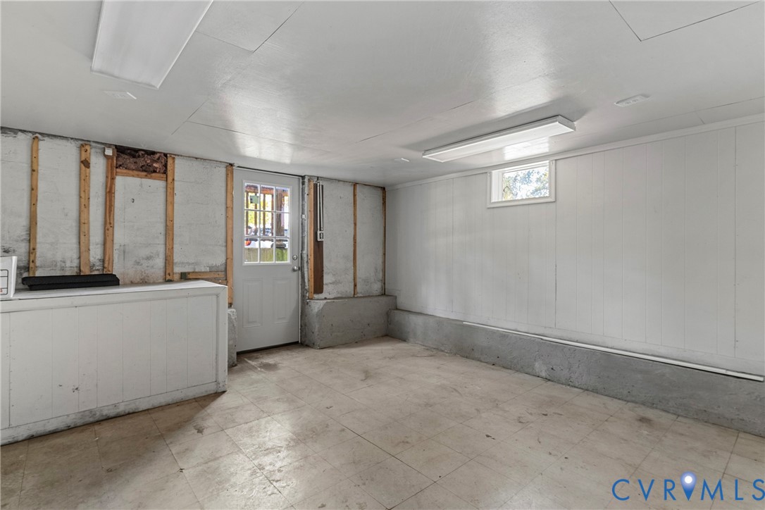 White paneling, concrete foundation, exterior access door with window panes, window with natural light, and overhead fluorescent lighting