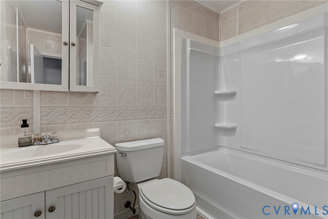 Bathroom featuring a white vanity with beadboard paneling, mirrored medicine cabinet, white porcelain toilet, and a white fiberglass tub with an integrated shower surround