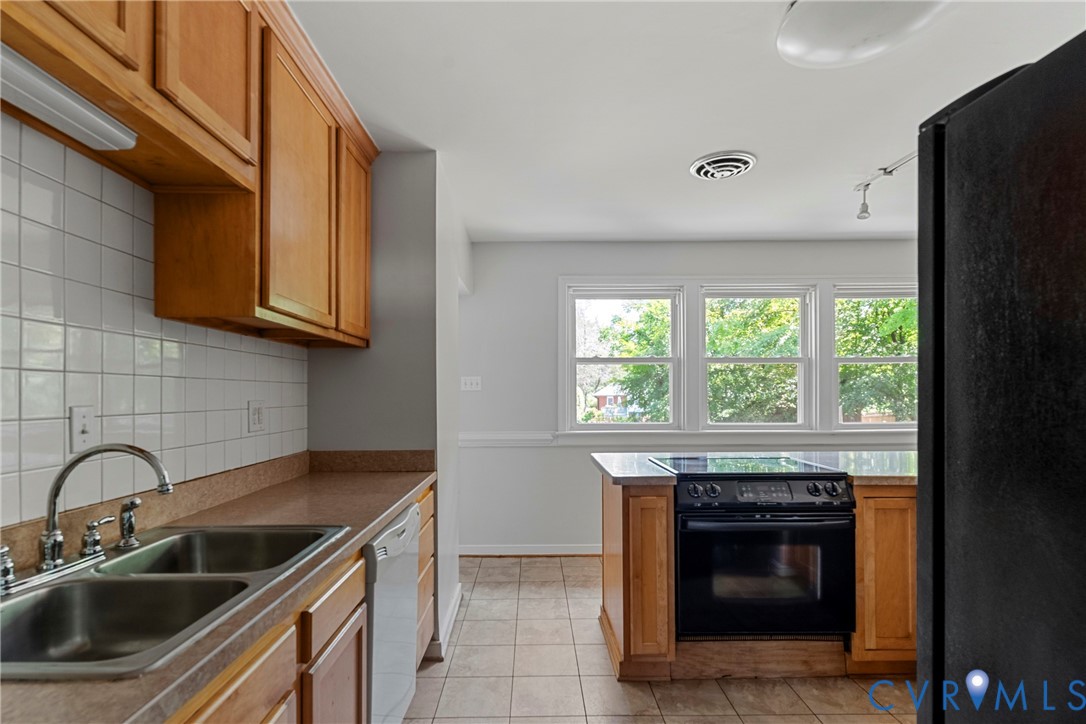 Kitchen featuring wood cabinetry, a double basin stainless steel sink, a tile backsplash, and a black range
