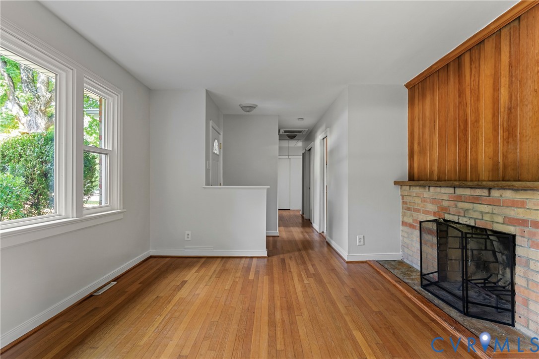 Hardwood flooring, brick fireplace, wood paneling accent wall, multiple windows with white trim, and a hallway with closet doors