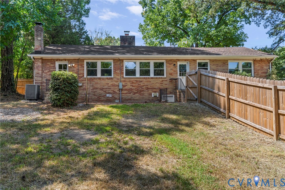 Brick exterior with multiple windows, a wooden privacy fence, a back door with stairs, and mature trees