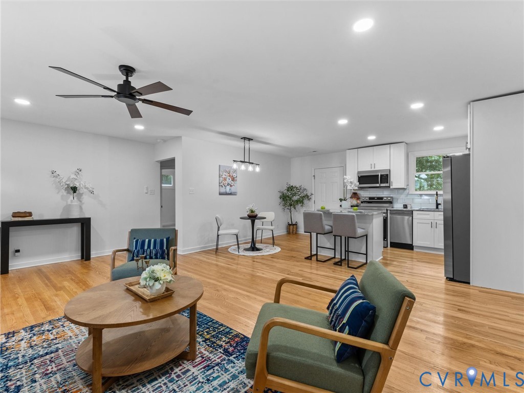 Wood-finish flooring throughout, recessed ceiling lighting, and a kitchen featuring stainless steel appliances, white cabinetry, and a tile backsplash