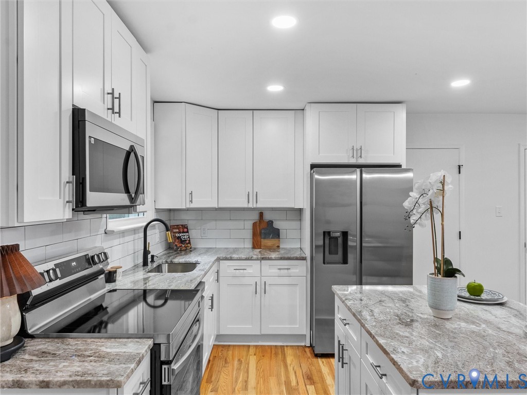 Modern kitchen featuring white shaker cabinetry, stainless steel appliances, light-toned countertops, subway tile backsplash, and wood-finish flooring