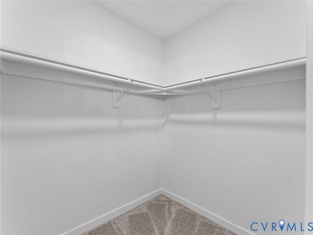 Walk-in closet featuring white wire shelving, white hanging rods, and neutral-toned carpeting
