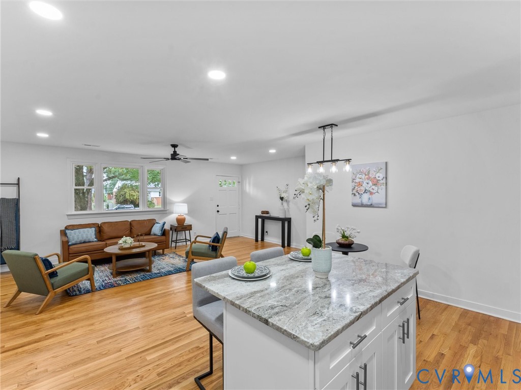 Open-concept living area featuring hardwood flooring, recessed lighting, and a white kitchen island with a stone countertop and seating