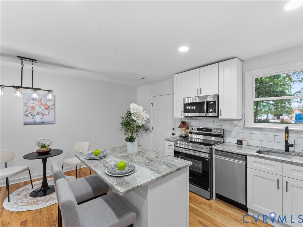 White cabinetry, stainless steel appliances, wood-finish flooring, light-colored countertops, and white subway tile backsplash