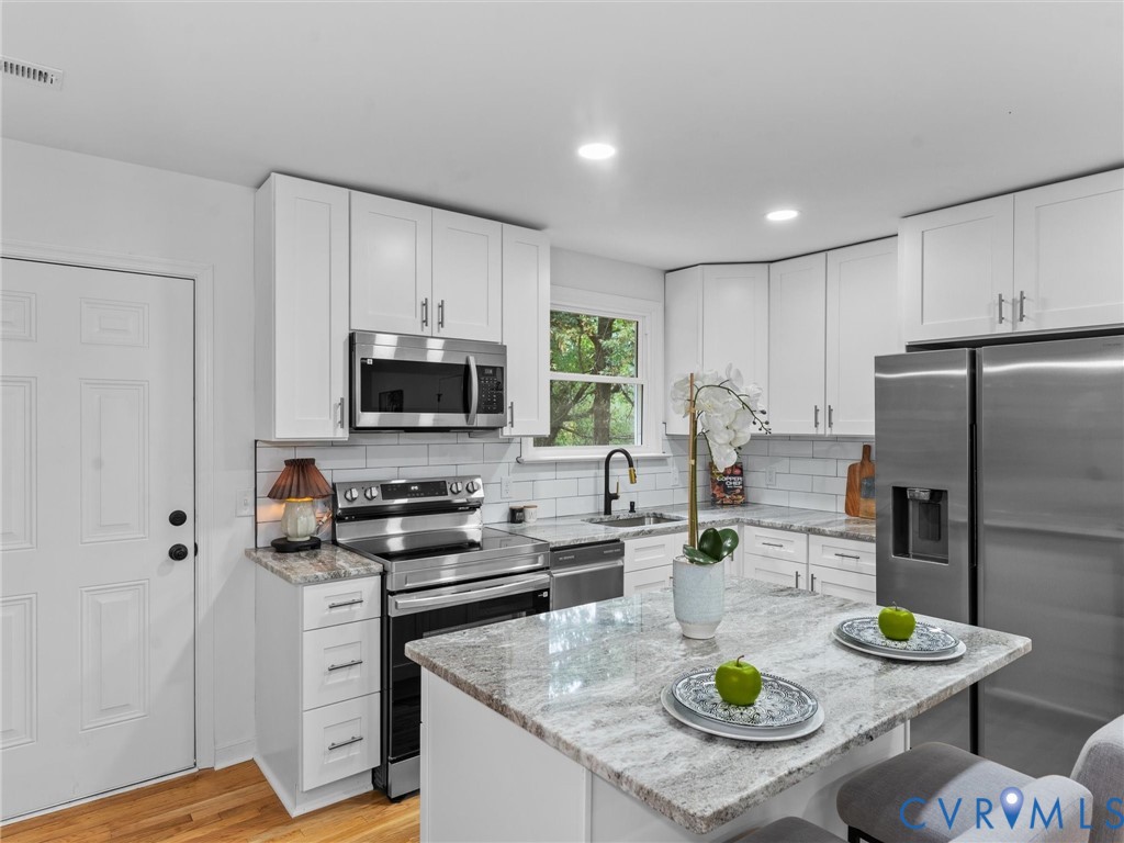White cabinetry, stainless steel appliances, granite countertops, subway tile backsplash, and an island with seating
