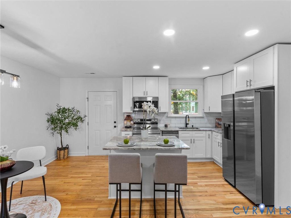 Kitchen with wood-finish flooring, white cabinetry, a central island with countertop seating, stainless steel appliances, and recessed lighting