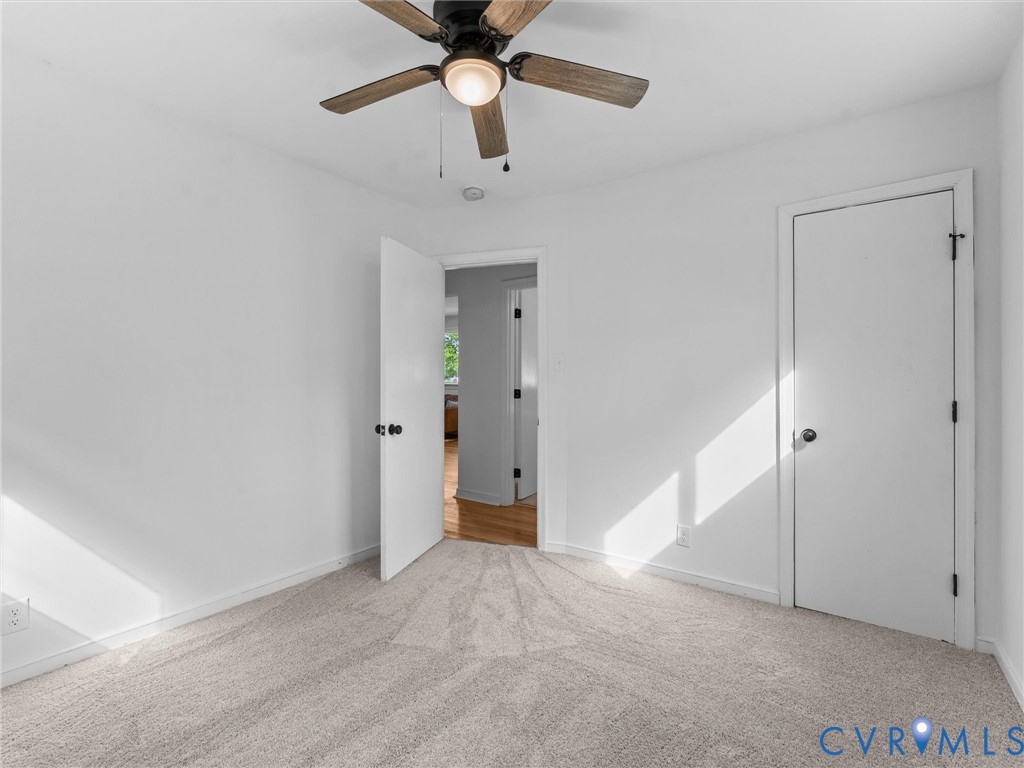Neutral-toned carpeting, white walls, and a ceiling fan with light fixture
