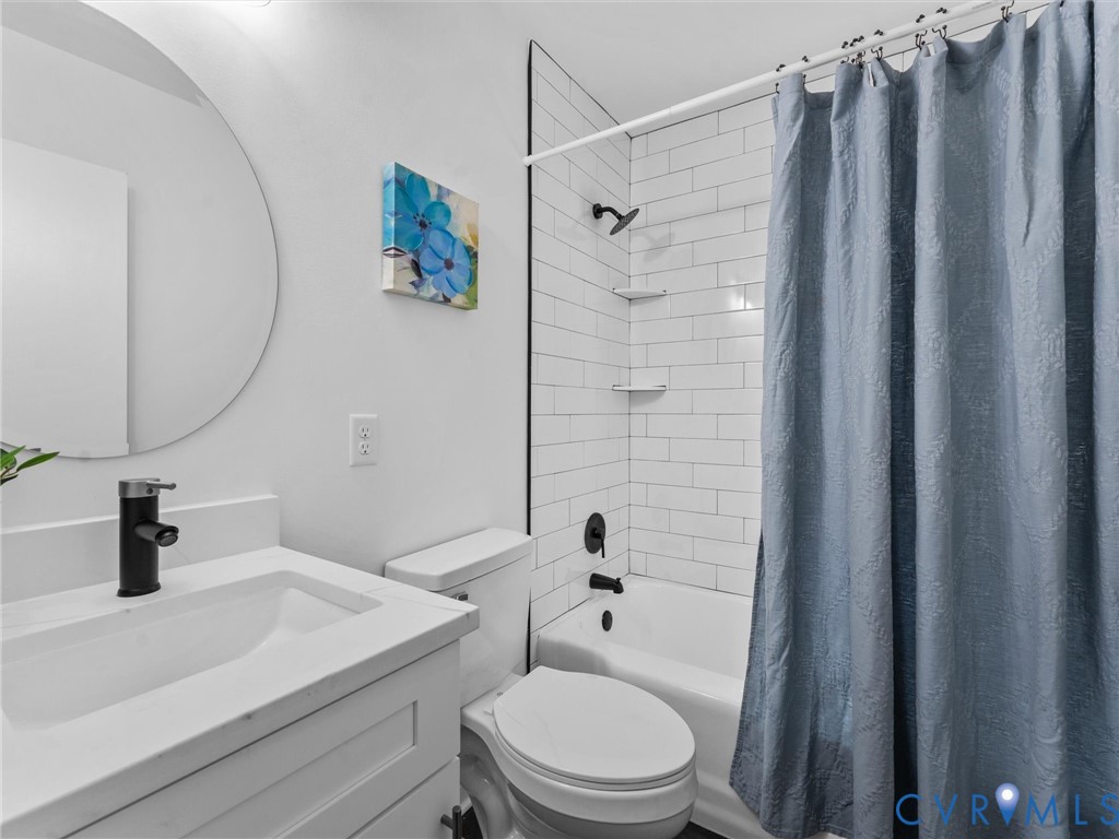 Full bathroom featuring a vanity with an integrated sink and matte black faucet, a circular wall mirror, and a tiled shower/tub combination with built-in shelving